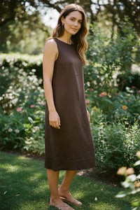 Button Down SF brown linen sleeveless midi dress with round neckline worn by a model in a garden setting.
