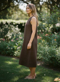 Button Down SF brown linen sleeveless midi dress with round neckline on a woman standing in a garden.